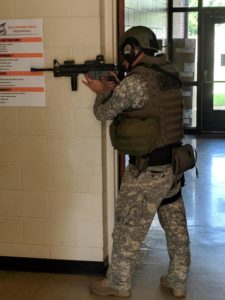 Camouflaged armed first responder in a hallway poised with a rifle